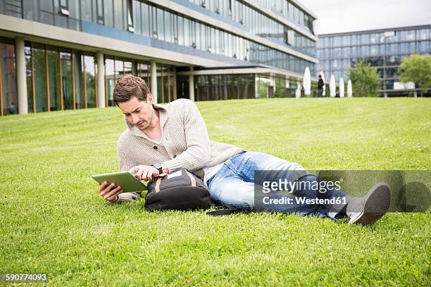 germany, tuebingen, young man relaxing on a meadow with digital tablet - tübingen stock pictures, royalty-free photos & images