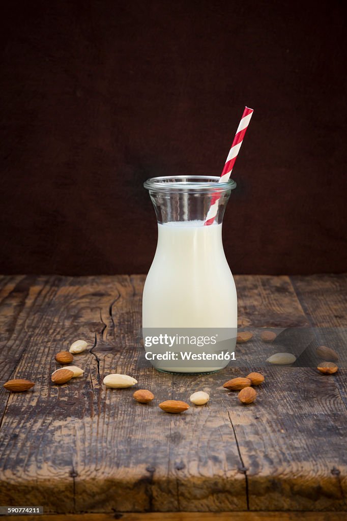 Almond milk in glass, drinking straw, on wood