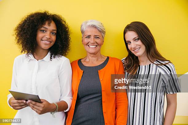 group picture of three smiling women standing in front of a yellow wall - close to stockfoto's en -beelden