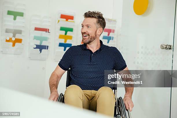 smiling man in wheelchair in modern office - wheelchair office stock pictures, royalty-free photos & images