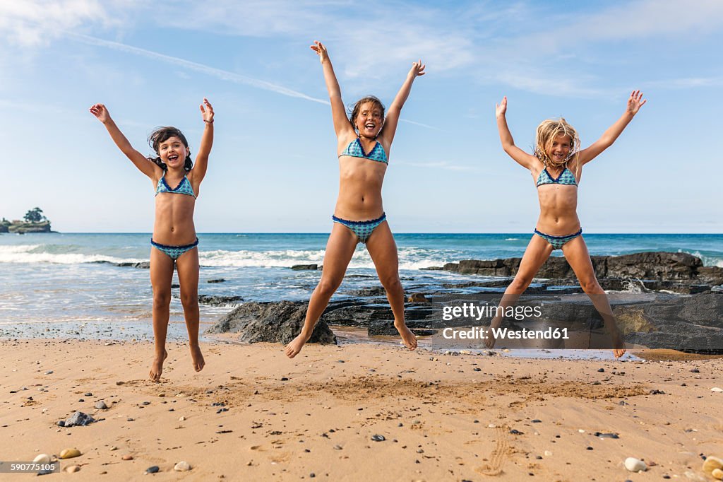 Spain, Colunga, three girls jumping in the air on the beach