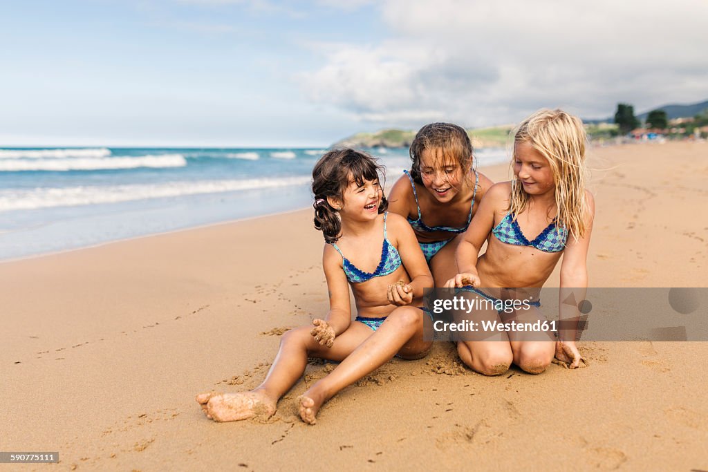 Spain, Colunga, three girls sitting on the beach having fun