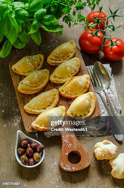 stuffed pastry with black olives, tomatoes and basil on wooden board - calzone stock-fotos und bilder