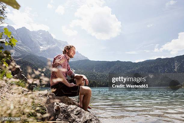 germany, bavaria, eibsee, smiling man in lederhosen sitting on lakeshore - berge bayern stock-fotos und bilder