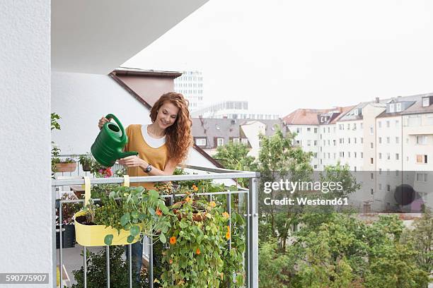 smiling woman watering flowers on balcony - balcony stock pictures, royalty-free photos & images