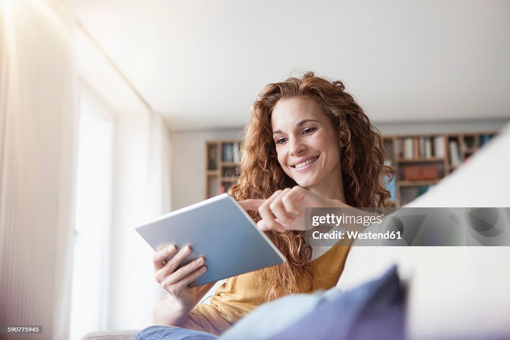 Smiling woman at home sitting on couch using digital tablet
