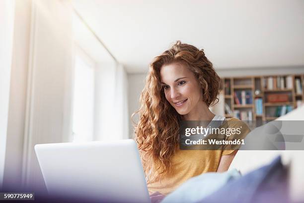 woman at home sitting on couch using laptop - 30 34 jaar stockfoto's en -beelden