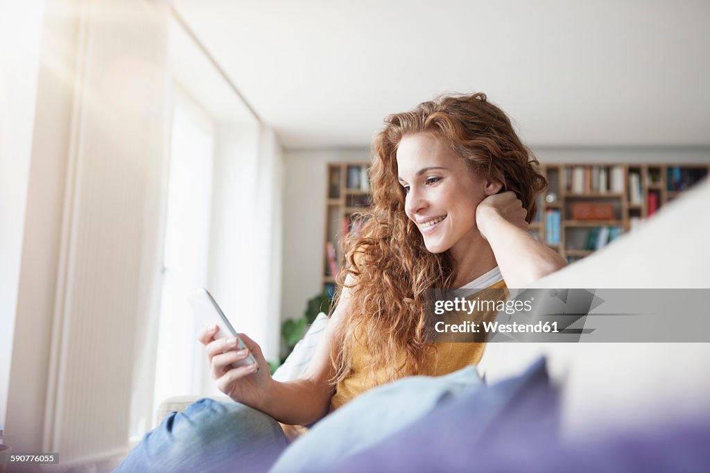 Smiling woman at home sitting on couch looking on cell phone