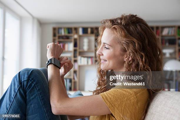 smiling woman at home sitting on couch looking at smartwatch - mens wrist watch stockfoto's en -beelden