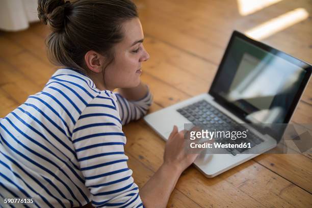 young woman at home lying on wooden floor, using laptop - touch pad stock pictures, royalty-free photos & images