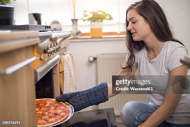young woman taking fresh pizza out of oven - oven glove stock pictures, royalty-free photos & images