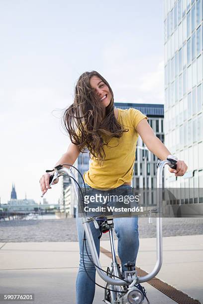 germany, cologne, portrait of smiling young woman with blowing hair on her bicycle - zusammenklappbar stock-fotos und bilder