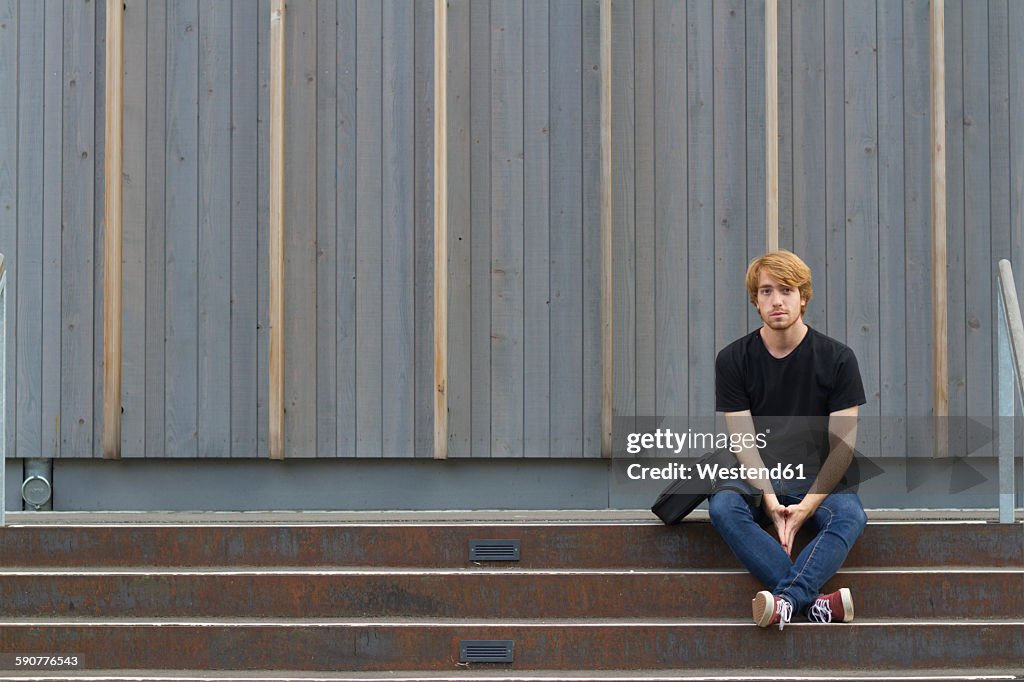 Young man sitting on steps in front of wooden facade