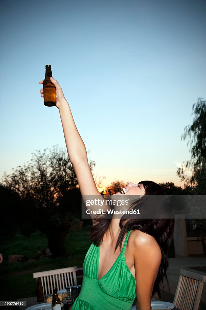 Happy young woman lifting a beer at sunset