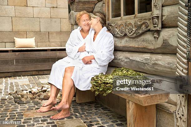 smiling senior couple in bathrobes sitting outside finnish sauna log cabin - the image bank stock-fotos und bilder
