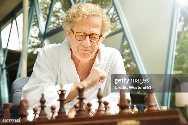 senior man in bathrobe playing chess - playing chess stock-fotos und bilder