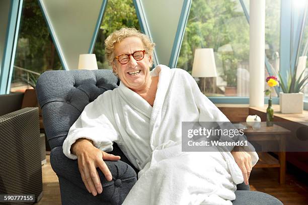 laughing senior man in bathrobe sitting in armchair - bathrobe fotografías e imágenes de stock