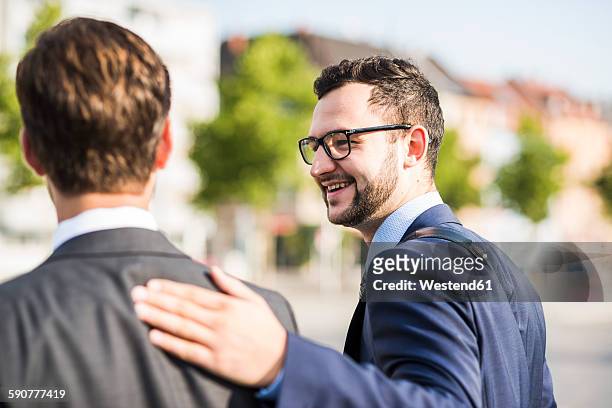 two young businessmen walking in city, one patting colleagues back - admiración fotografías e imágenes de stock