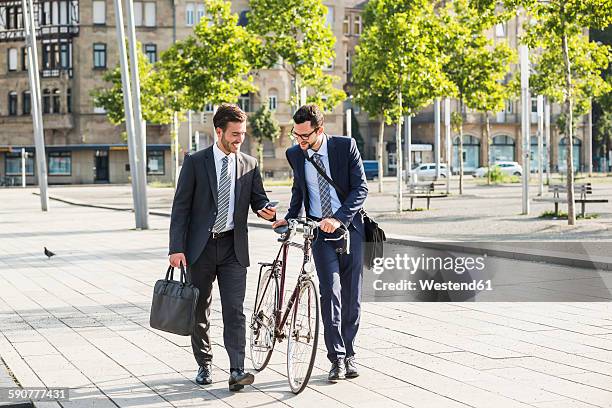 two businessmen with bike and smart phone walking in the city - a buisness man with a brifecase stock-fotos und bilder
