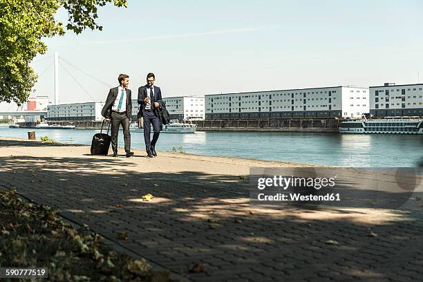 two young businessmen on a business trip, walking by river - ludwigshafen stockfoto's en -beelden