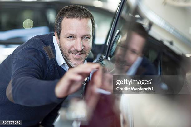 smiling man examining new car at car dealership - blank expression stock-fotos und bilder