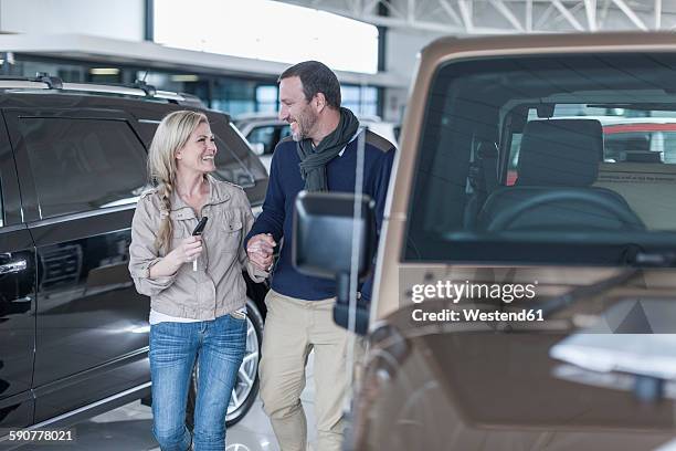 happy couple at car dealership hand in hand at new car - car keys hand ストックフォトと画像