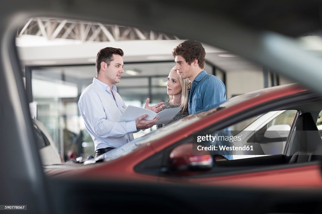 Car dealer showing brochure to young couple in showroom