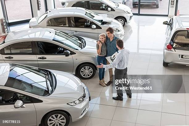 car dealer showing new car to young couple in showroom - venditore di automobili foto e immagini stock