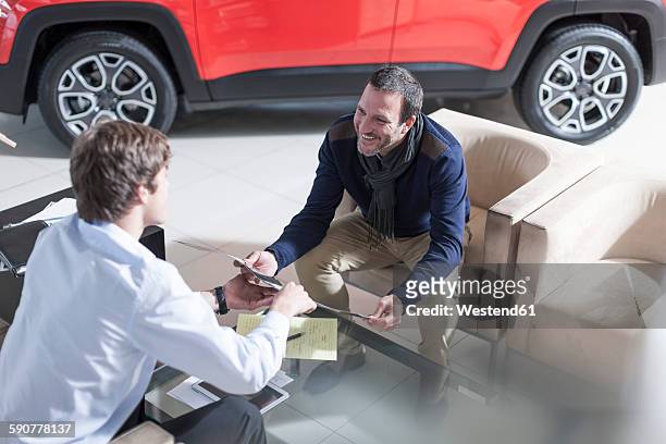 man at car dealership looking at brochure - car dealership stock pictures, royalty-free photos & images