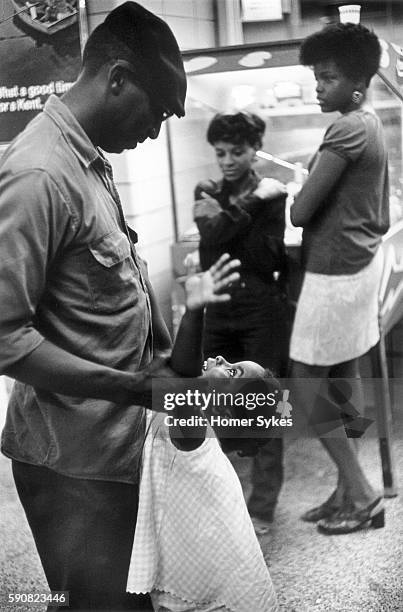 WASHINGTON DC LATE AT NIGHT IN A GREYHOUND BUS STATION, AN AFRICAN AMERICAN FATHER AND HIS YOUNG DAUGHTER PLAY TOGETHER, WHILE TWO OLDER SISTERS LEAN...