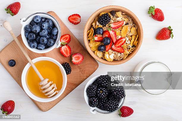 healthy breakfast with cereal, fresh berries, yogurt and honey over white rustic wooden table viewed from above - cereal bowl stockfoto's en -beelden