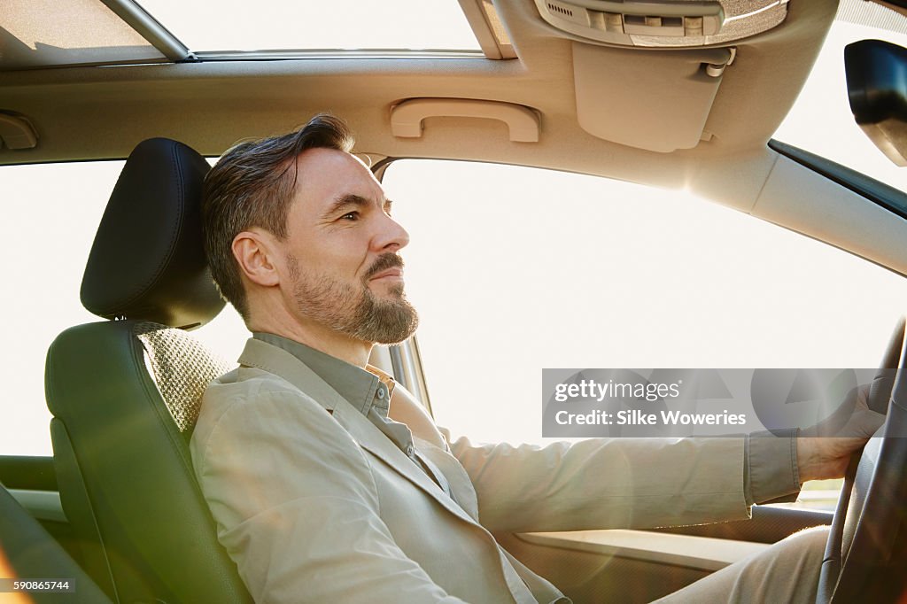 Middle-aged man sitting in his car driving at sunset
