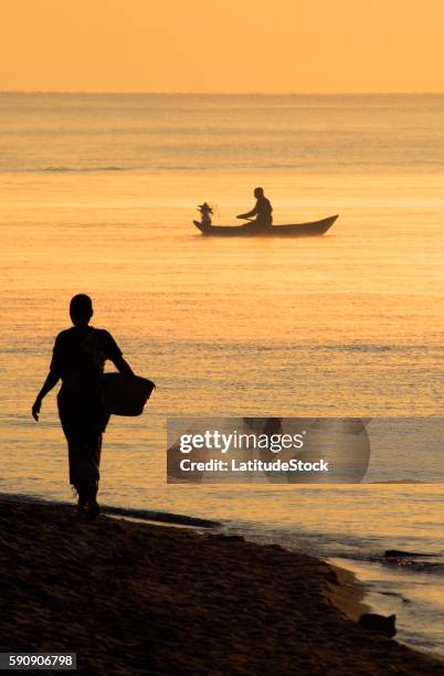 fishermen in a canoe and woman walking along the shore at sunrise by lake malawi - malawi stock pictures, royalty-free photos & images