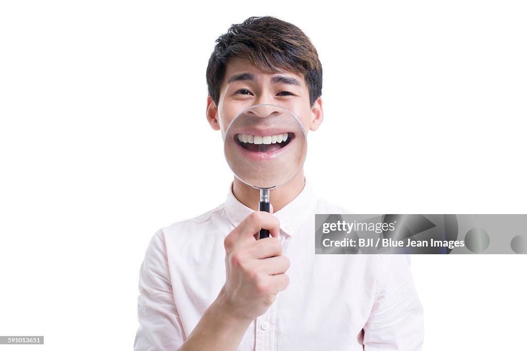 Young man holding a magnifying glass in front of his mouth