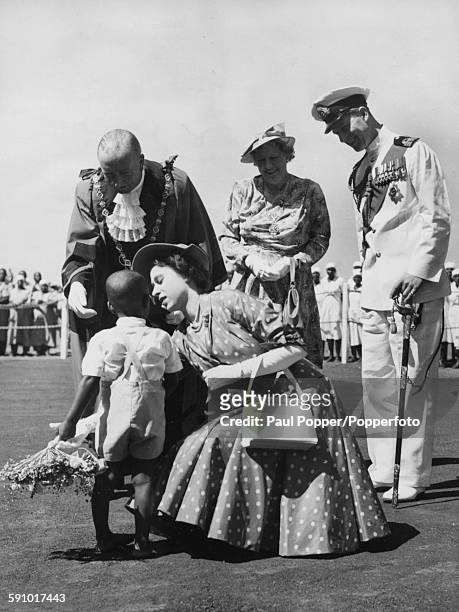 Princess Elizabeth crouches down to receive a bouquet from young Prince Selim, watched by the Mayor of Nairobi , Alderman J R Maxwell, his wife and...