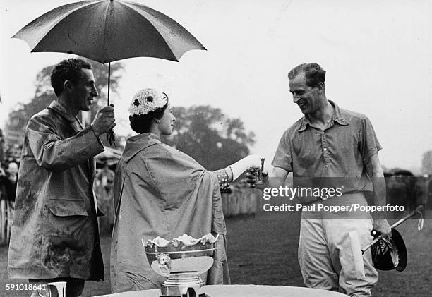 Queen Elizabeth II presents a cup to her husband, Prince Philip, Duke of Edinburgh as captain of the winning team after the novice polo final match...