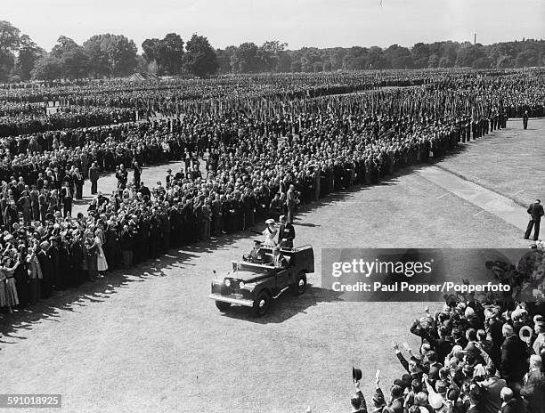 Queen Elizabeth II and Prince Philip, Duke of Edinburgh wave from the back of an open Land Rover as they drive past long lines of ex-servicemen at a...