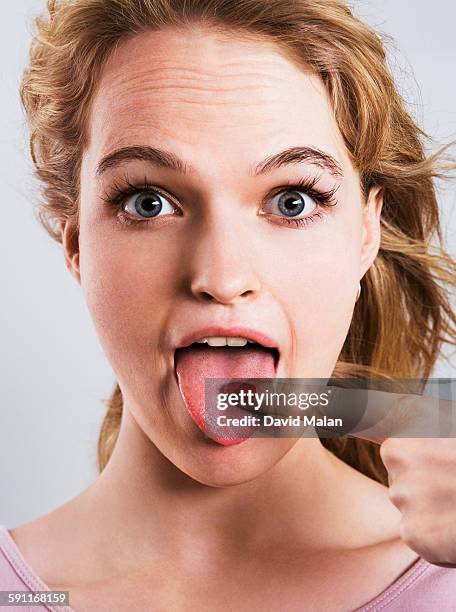 young blonde woman pointing at her tongue - tongue out stockfoto's en -beelden