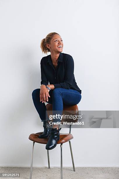 portrait of smiling woman on backrest of a chair in front of white background - sitting in a chair stockfoto's en -beelden