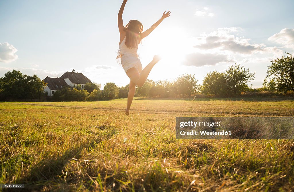 Back view of woman jumping in the air on a meadow at backlight