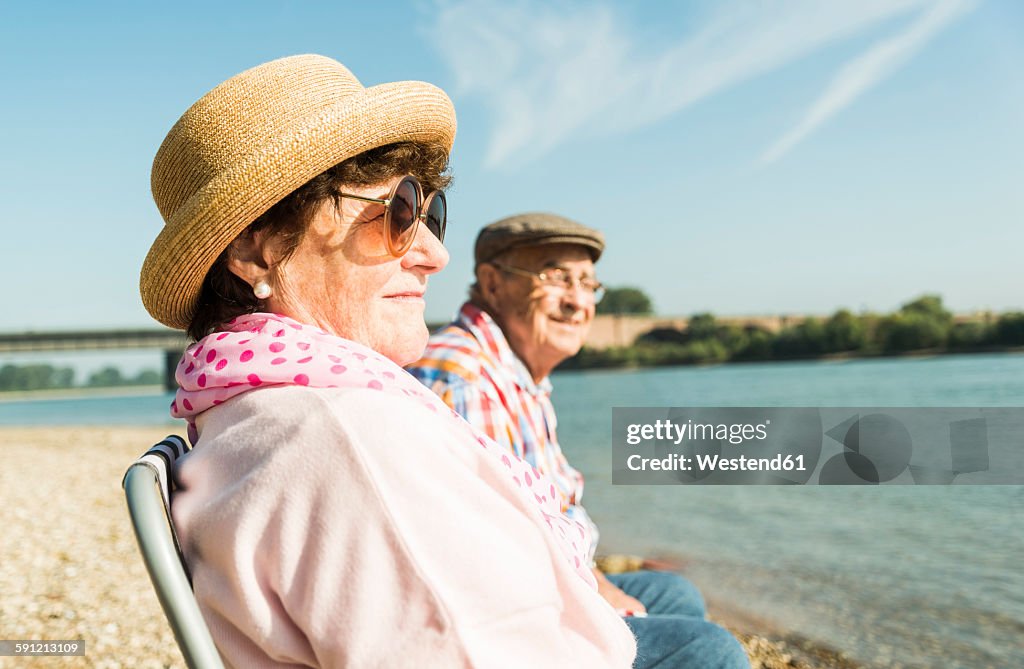 Germany, Ludwigshafen, senior couple sitting on folding chairs at riverside