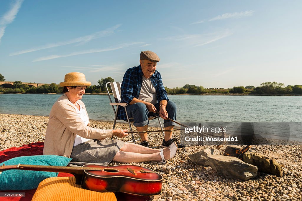 Germany, Ludwigshafen, senior couple barbecueing sausages on the beach