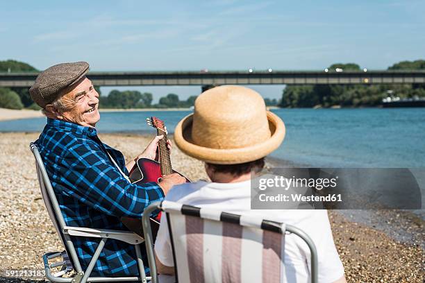 germany, ludwigshafen, senior couple with guitar at riverside - folding chair stock-fotos und bilder