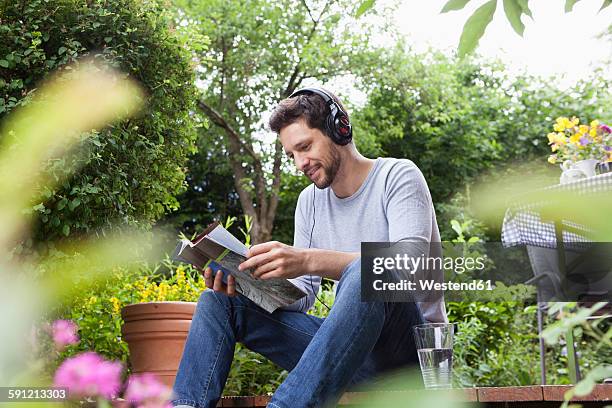 relaxed man sitting in garden with headphones and magazine - nature magazine stock pictures, royalty-free photos & images