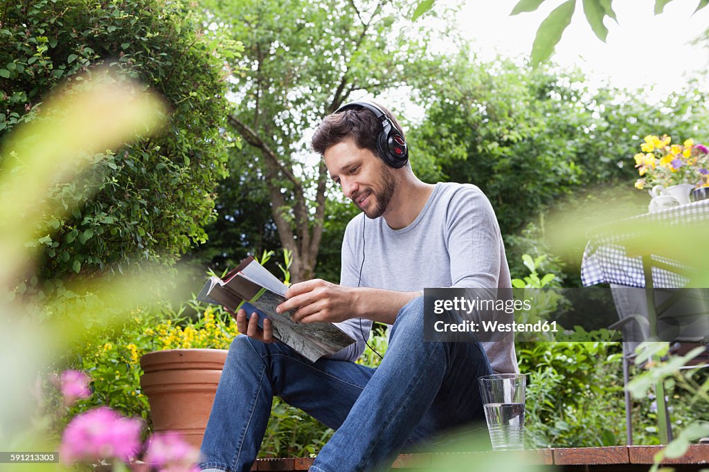 Relaxed man sitting in garden with headphones and magazine