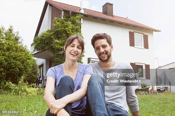 portrait of smiling couple in garden in front of residential house - bavarian man in front of house stock-fotos und bilder