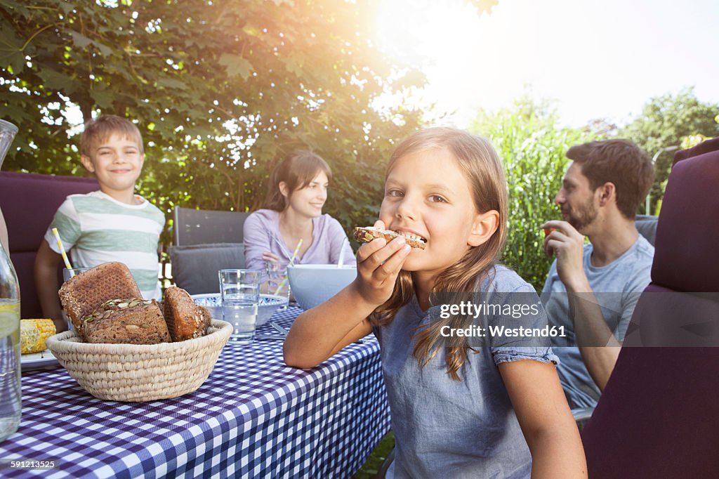 Girl eating bread with family at garden table