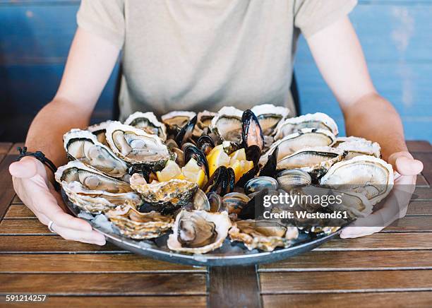 man's hands holding a seafood platter with oysters, clams and mussels. - seafood platter stock pictures, royalty-free photos & images