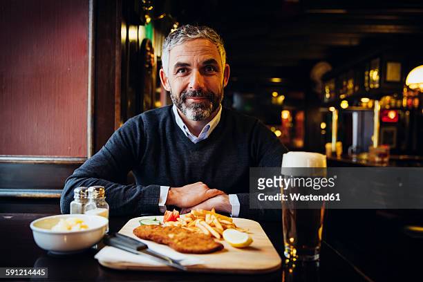smiling man in restaurant having wiener schnitzel with french fries - gast stock-fotos und bilder