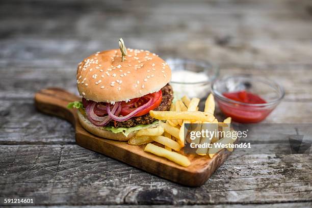 homemade burger with lettuce, meat, tomato, onion and french fries on chopping board - french fries stock pictures, royalty-free photos & images